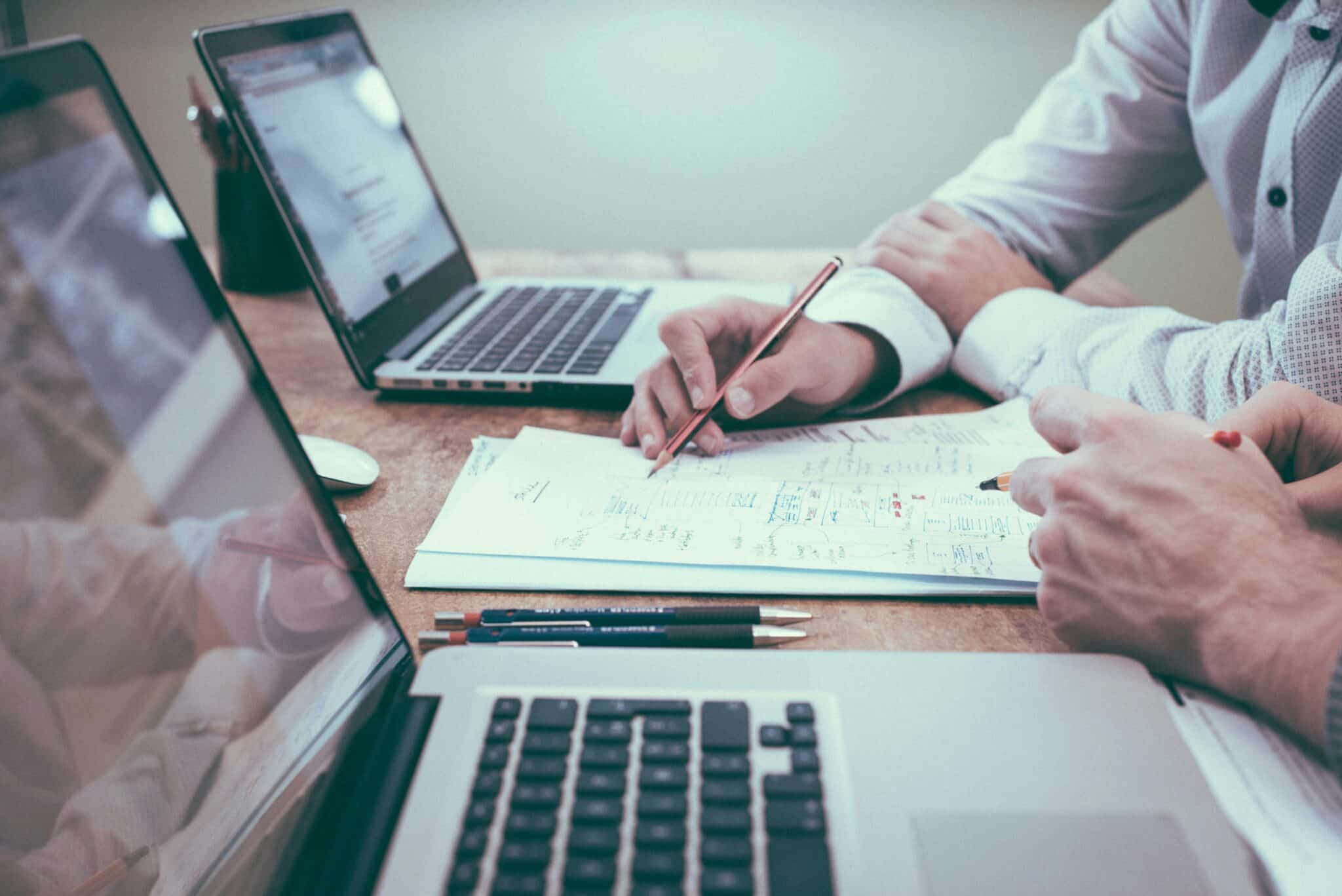 Two people working on documents and laptops on a desk