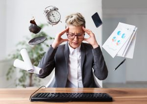Mature women with pixie cut stressed out at work at her desk because she's trying to work and multi-tasking doesn't work