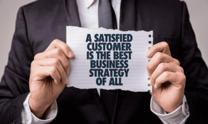 A man in a business suite holding a piece of paper that says a satisfied customer is the best business strategy of all