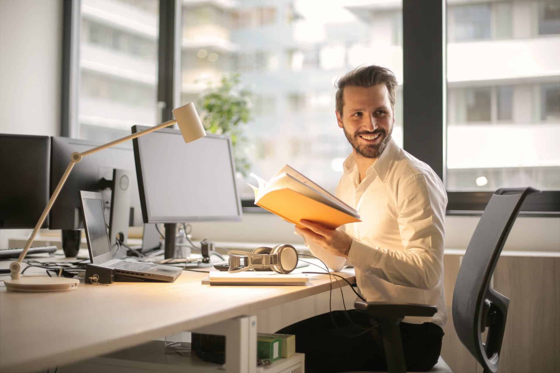 Man holding a book while sitting on a desk
