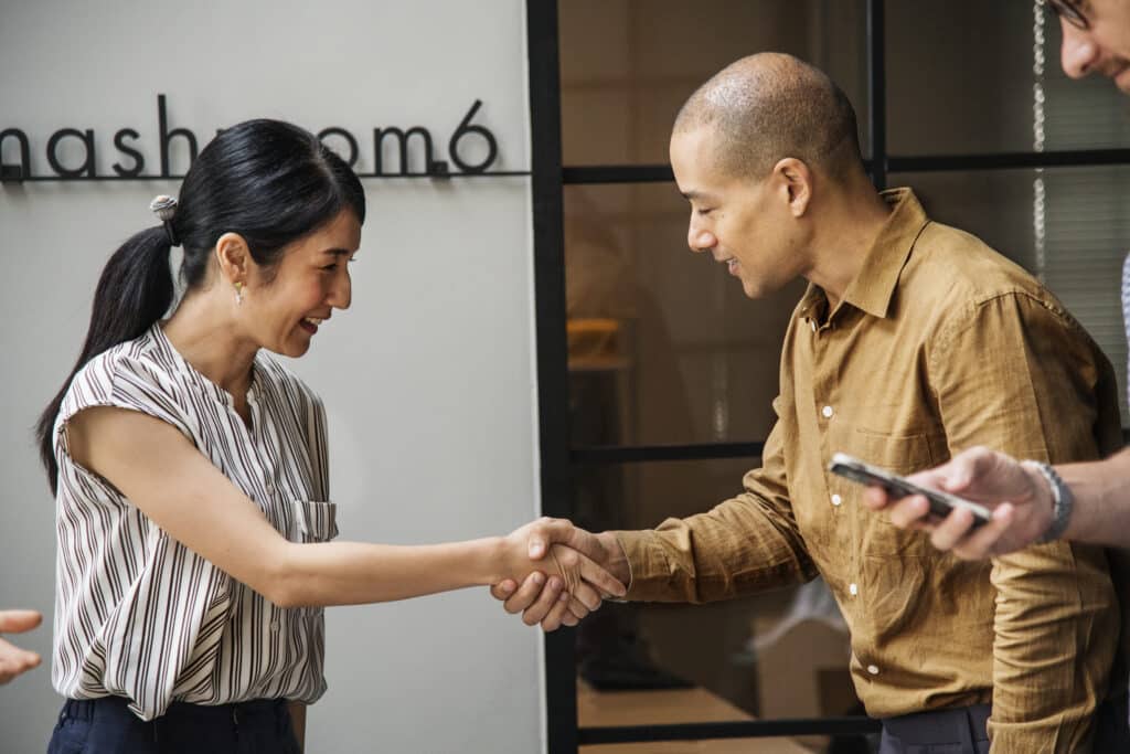 Two business professionals shaking hands in an office setting, smiling during a meeting