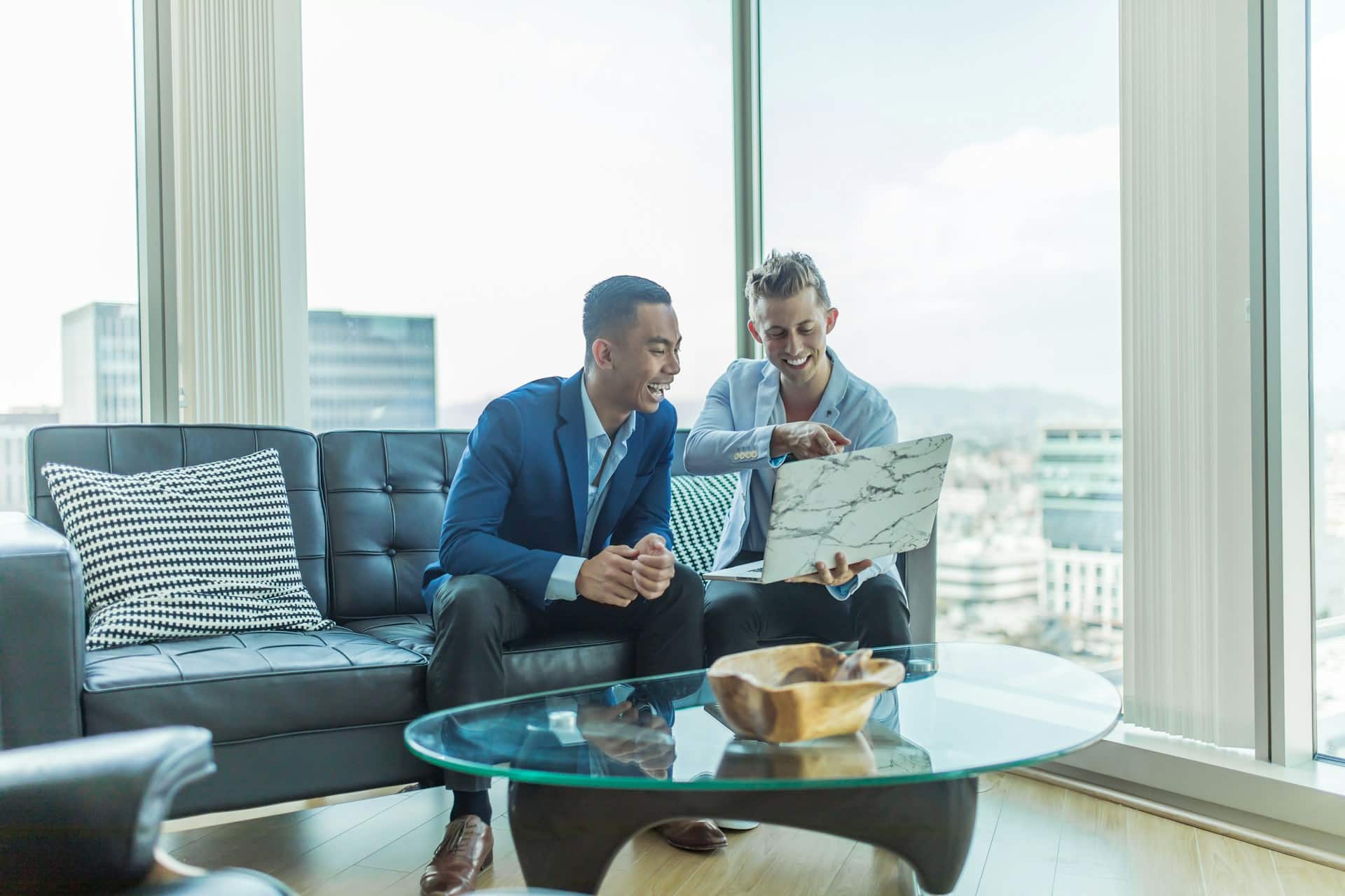 Two men sitting on a sofa in front of a laptop