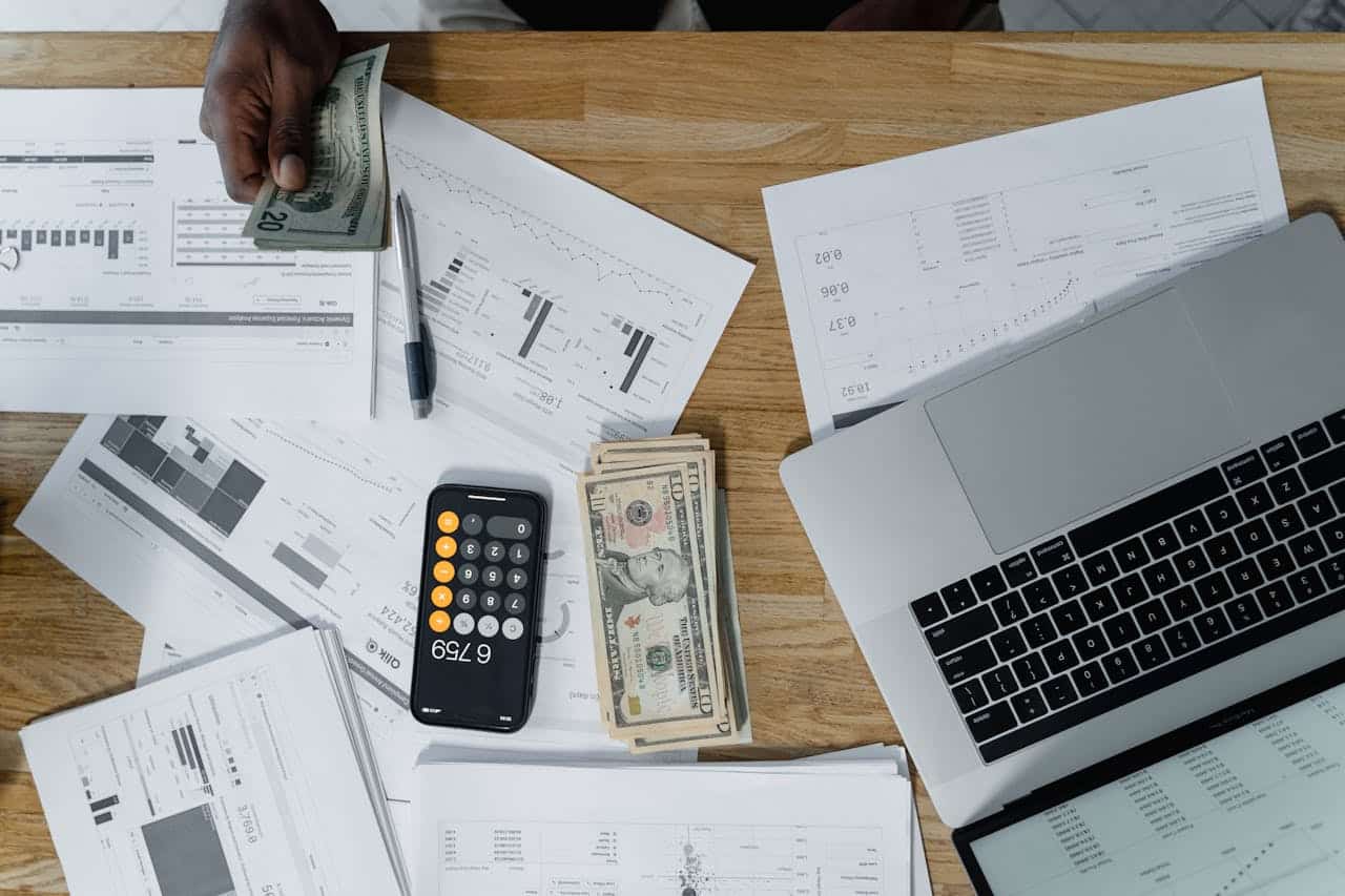 Someone counting money at a desk with charts, cash, and a laptop, showing business finances