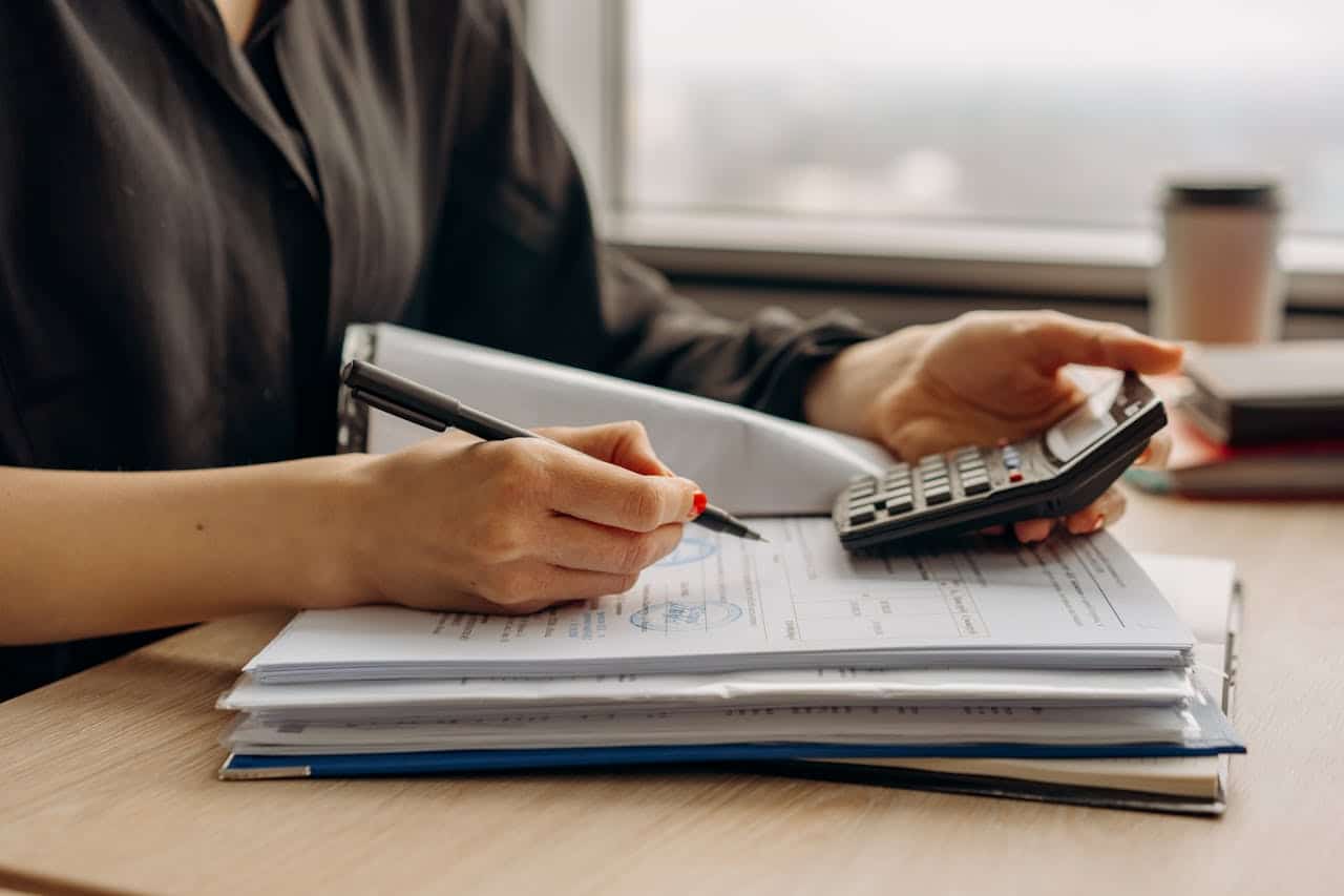 person writing on a notebook while holding a calculator