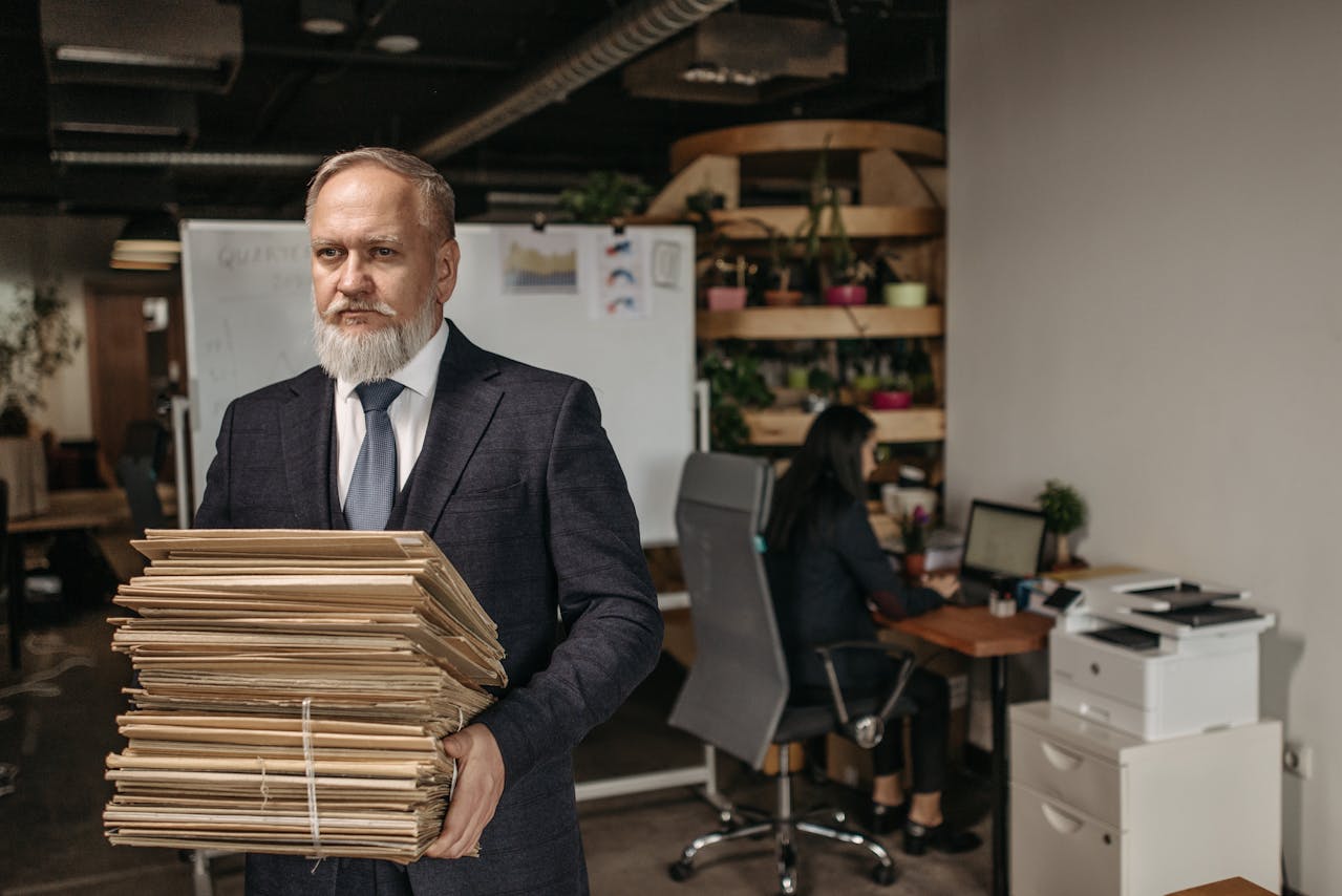 An elderly man carrying a stack of brown envelopes