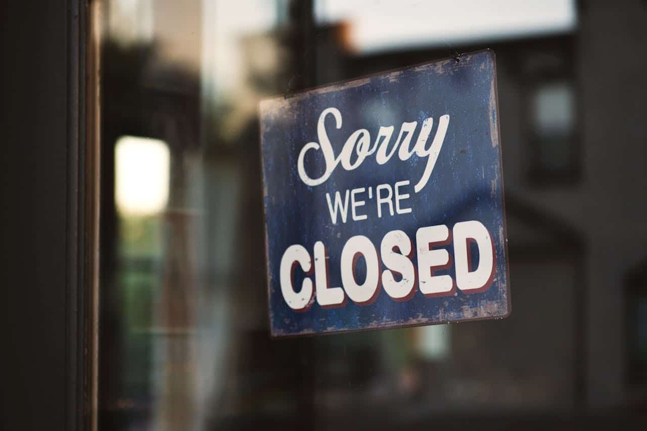 A “Sorry We’re Closed” sign placed against a glass door