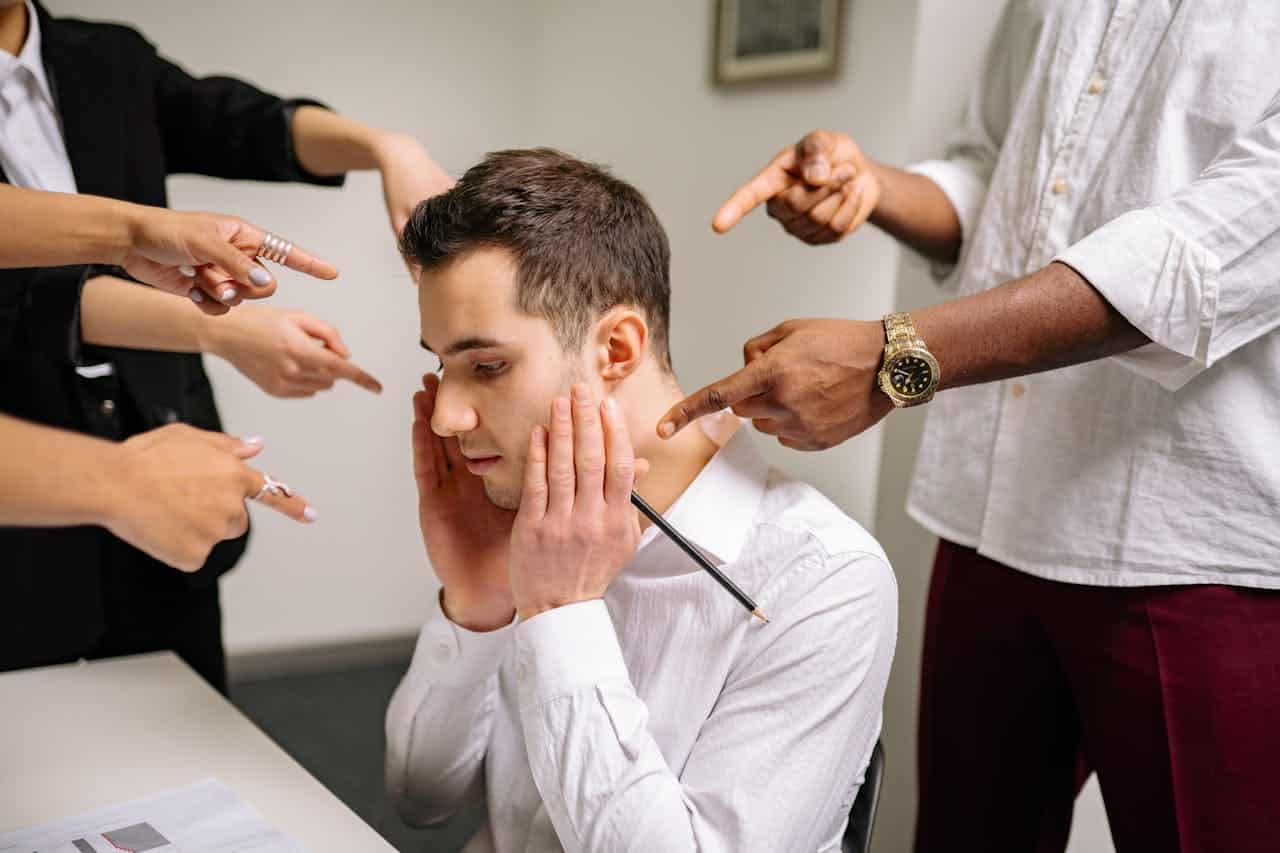 People pointing their fingers to a man sitting in his chair
