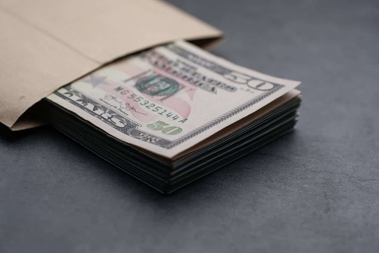 A stack of dollar bills peeking out of a brown envelope