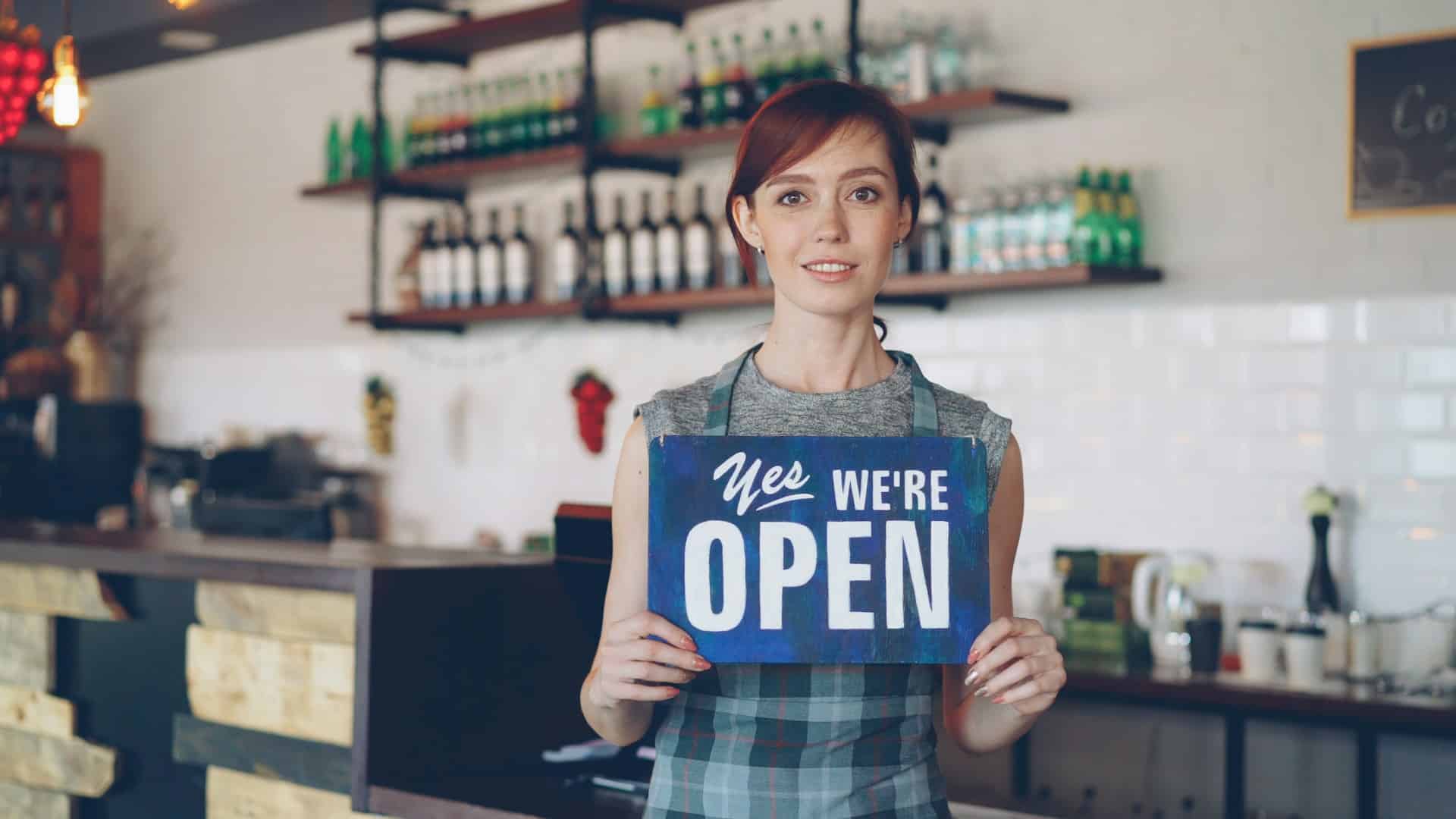 A woman holding a “Yes, We’re Open” sign