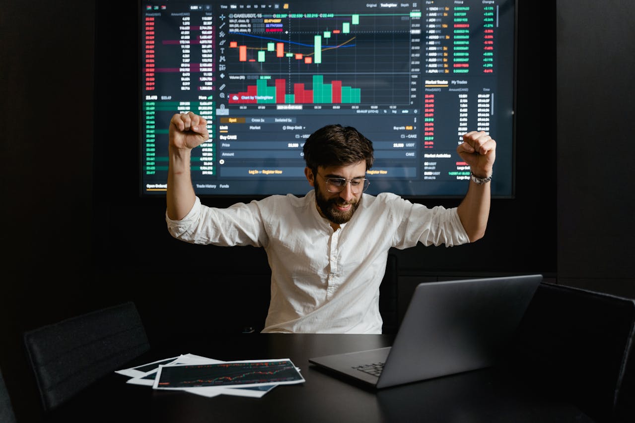A trader raising his arms in front of his computer