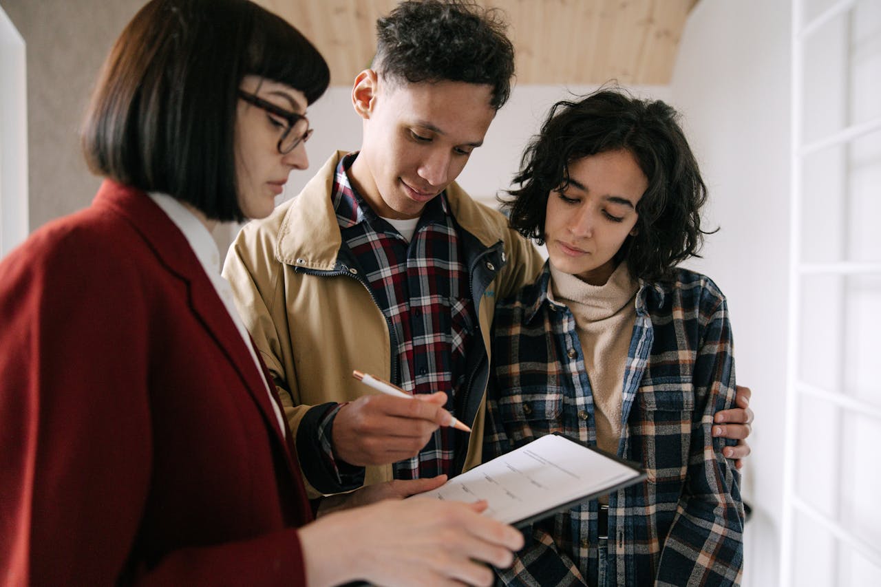 A couple signing a document held by a female real estate agent