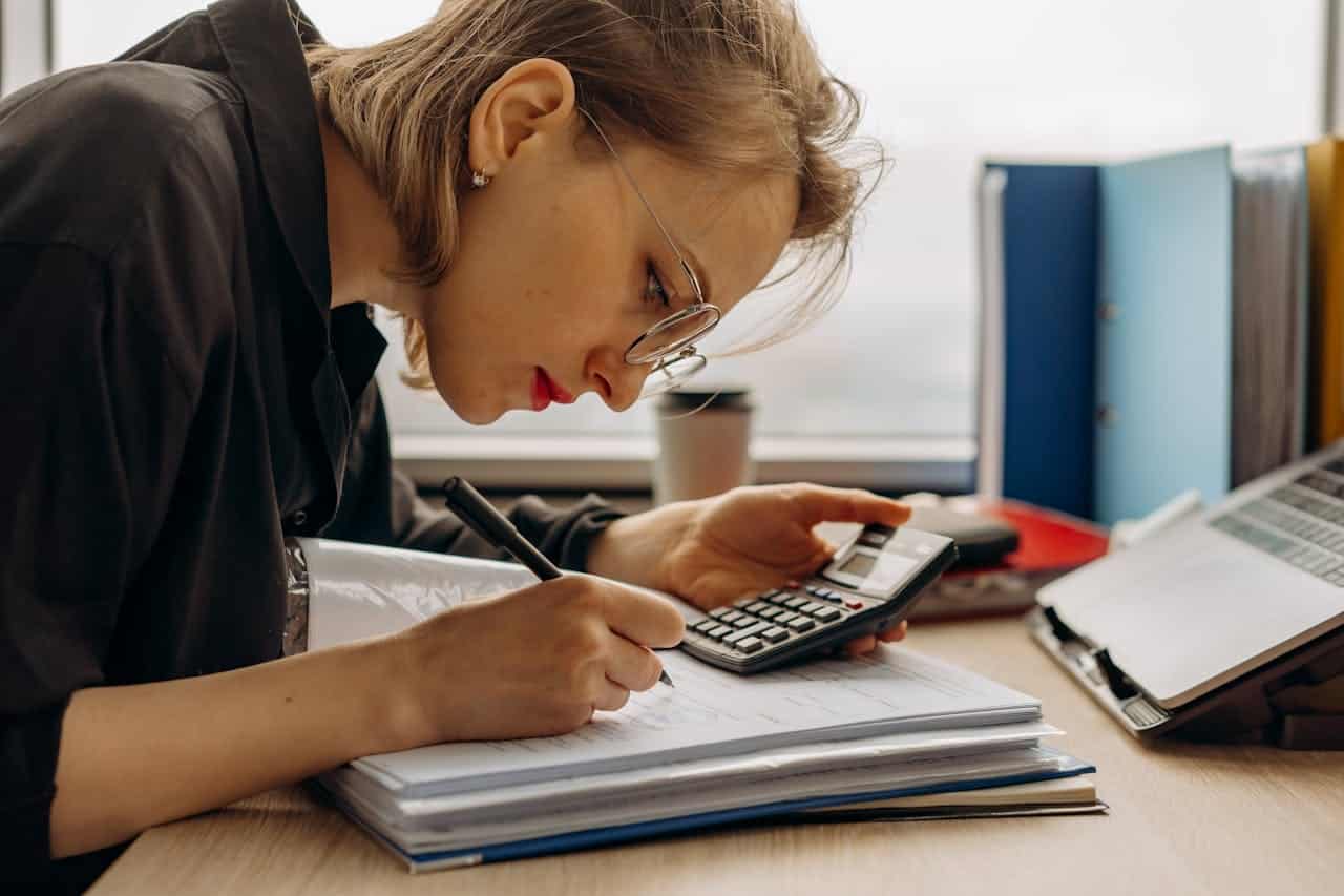 Business owner calculating startup and filing expenses using a calculator and ledger