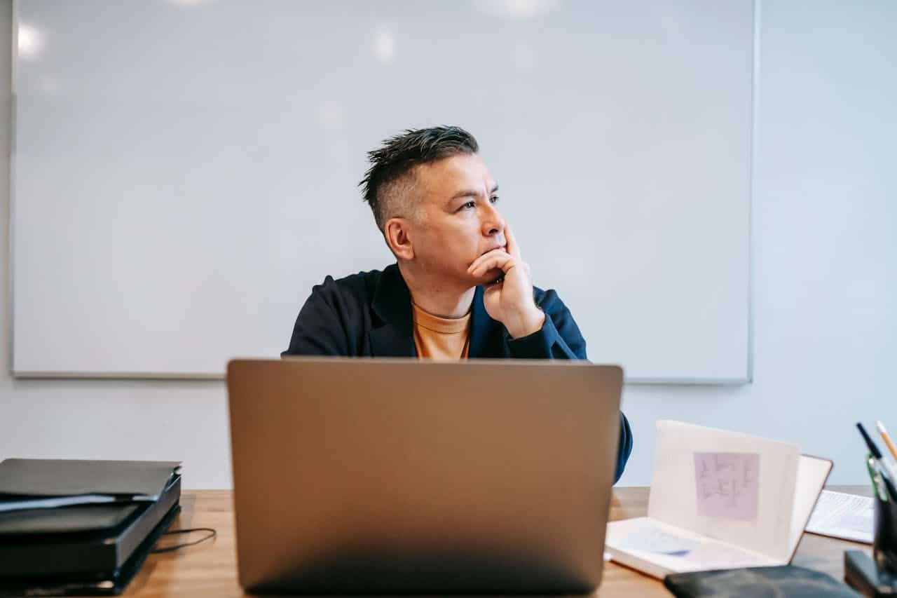 A man looking away from his computer with one hand on his chin