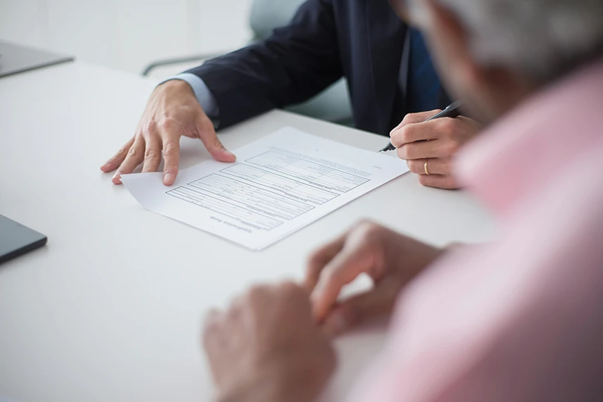 A man in a suit signing documents on an office table.
