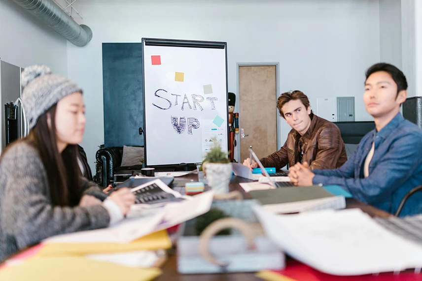 People gathered in a meeting room with &ldquo;Start-Up&rdquo; written on a whiteboard.