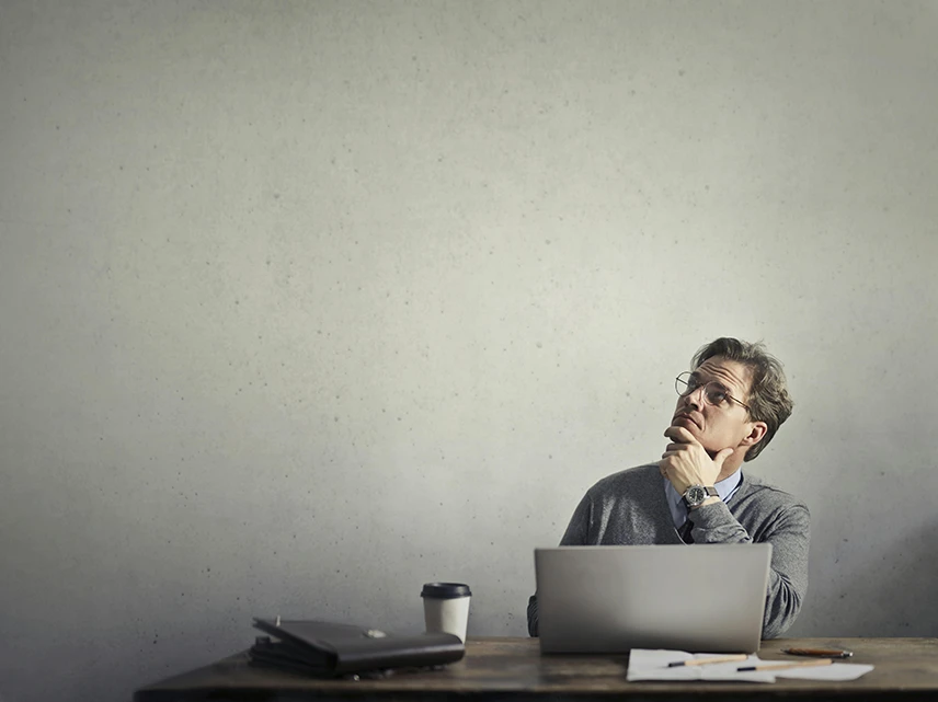  A man in office attire using his laptop while rubbing his chin and thinking.